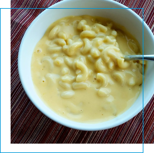 A white bowl filled with creamy macaroni and cheese sitting in a maroon table cloth